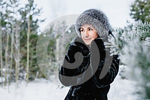 Portrait of attractive smiling young woman in worm hat in wintertime outdoor. Girl in winter forest