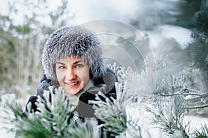 Portrait of attractive smiling young woman in worm hat in wintertime outdoor. Girl in winter forest