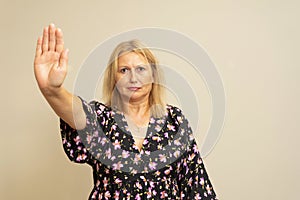 Portrait of attractive strict fair-haired woman showing palm stop sign decision isolated over beige background.