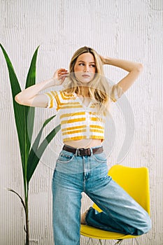 Portrait of attractive stylish caucasian young woman with blonde hair posing near yellow chair
