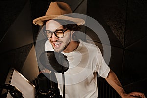 Portrait of attractive stylish male musician confidently singing in microphone recording song in professional studio