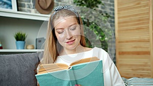 Portrait of attractive teenage girl reading book at home smiling turning pages