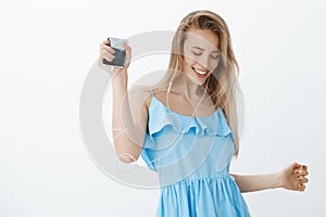 Portrait of attractive tender and sincere female with blond hair in blue dress jumping and dancing carefree as listening