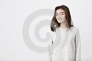 Portrait of attractive trendy female student with lifted eyebrows, smiling anxiously while looking at camera over white
