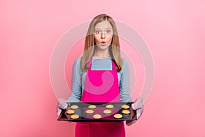 Portrait of attractive trendy funny amazed girl holding tray fresh baked cookies isolated over pink pastel color