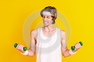 Portrait of attractive weak sportive guy lifting weight working out doing effort isolated over bright yellow color