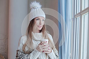 Portrait of attractive winter woman in season casual clothes white sweater and knitted hat at cozy home