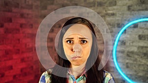 Portrait of attractive woman biting her lips resentfully against illuminated wall.