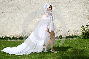Attractive woman, dressed in white, with veil, strides in front of a white wall photo