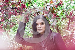 Portrait of attractive woman with long brown hair in leather jacket in garden with blossom red apple tree flowers and drops of