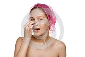 Portrait of attractive woman in pink cap touches her nose with plasters after rhinoplasty against white studio