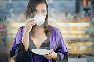 Portrait of attractive woman in a purple nightgown and silk robe holding a white cup of tea on a white background.