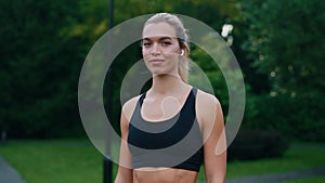 Portrait of the attractive woman runner standing in the park looking at the camera wearing earphones and sport clothes