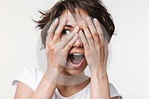 Portrait of attractive woman with short brown hair in basic t-shirt covering her eyes with hands