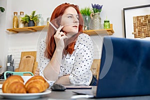 portrait of attractive woman sits in front of a computer in the kitchen. blogger writes a post on the internet. content