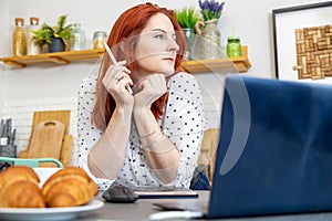 Portrait of attractive woman sits in front of a computer in the kitchen. blogger writes a post on the internet. content author,