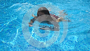 Portrait of attractive woman swimming in pool with blue clear water in warm summer day. Young girl relaxing during