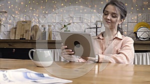 Portrait of an attractive woman using her touchpad and reading something while sitting in the kitchen against decorated