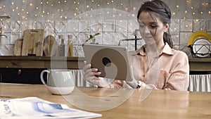 Portrait of an attractive woman using her touchpad and reading something while sitting in the kitchen against decorated