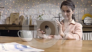 Portrait of an attractive woman using her touchpad and reading something while sitting in the kitchen against decorated