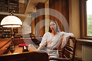 Portrait of an attractive woman in a white blouse sitting at a public library at a table and posing for the camera