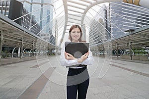 Portrait of attractive young Asian business woman holding document folder at sidewalk of urban city background.