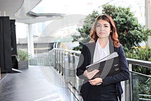 Portrait of attractive young Asian business woman holding document folder and walking in office.