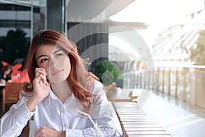 Portrait of attractive young Asian business woman talking on phone and waiting for partnership or somebody in cafe against copy sp