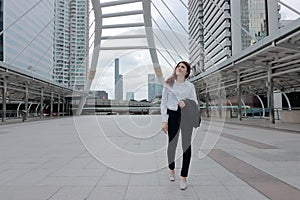 Portrait of attractive young Asian business woman walking and looking far away at sidewalk of urban city background.