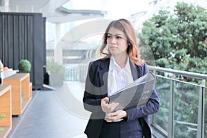 Portrait of attractive young Asian businesswoman or secretary holding document folder and walking in office.