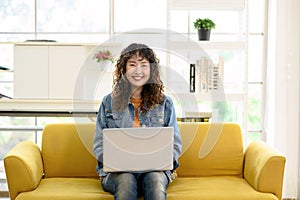 Portrait of attractive young Asian female graphic designer looking at the camera while working with laptop computer sitting on