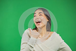 Portrait of an attractive young asian woman smiling looks away and showing thumbs up over green background