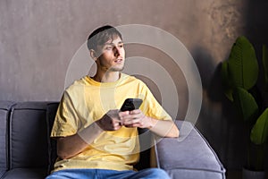 Portrait of an attractive young bearded man wearing casual clothes sitting on a couch at the living room, using mobile phone