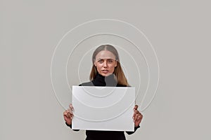 Portrait of attractive young caucasian woman looking at camera, holding white blank banner in front of her while