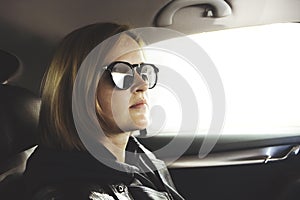 A portrait of attractive young Caucasian woman in sunglasses travelling in her car on the back seat