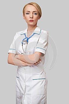 Portrait of an attractive young female doctor nurse in white coat over light grey background