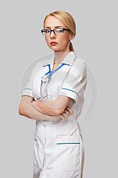 Portrait of an attractive young female doctor nurse in white coat over light grey background