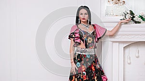 Portrait of an attractive young Gypsy woman standing near a decorative fireplace