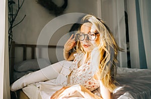 Portrait of attractive young happy caucasian woman in glasses, sitting in cozy bedroom