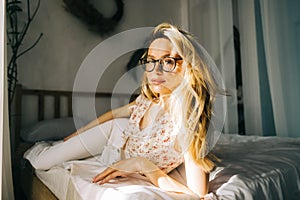 Portrait of attractive young happy caucasian woman in glasses, sitting in cozy bedroom