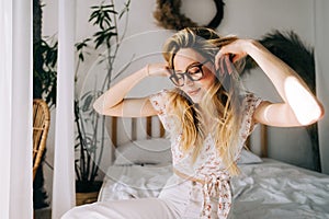 Portrait of attractive young happy caucasian woman in glasses, sitting in cozy bedroom