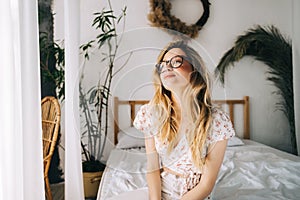 Portrait of attractive young happy caucasian woman in glasses, sitting in cozy bedroom