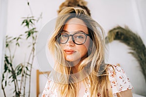 Portrait of attractive young happy caucasian woman in glasses, sitting in cozy bedroom