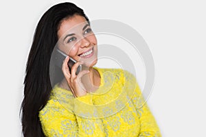 Portrait of attractive young happy woman with smart phone, wearing yellow sweater, with pretty toothy smile, on the white wall