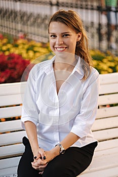 Portrait of attractive young lady in forma outfit sitting on bench in centre of city.