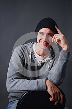 Portrait of an attractive young male model in black hat, jeans and gray sweatshirt, studio, dark gray background