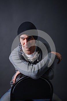 Portrait of an attractive young male model in black hat, jeans and gray sweatshirt, studio, dark gray background