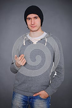 Portrait of an attractive young male model in black hat, jeans and gray sweatshirt, studio, dark gray background