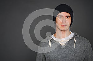 Portrait of an attractive young male model in black hat, jeans and gray sweatshirt, studio, dark gray background