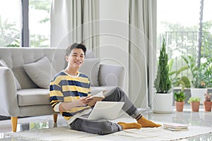 Portrait of an attractive young man sitting on a floor at the couch in the living room, using laptop computer
